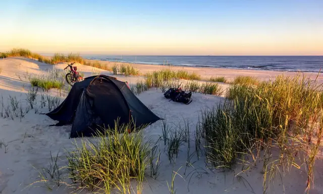 Namiot i rower na plaży, idealne miejsce na dzikie pola namiotowe. Morze i niebo w tle.