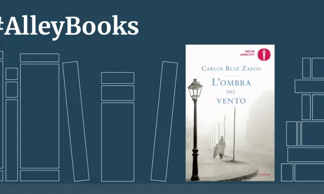 Copertina del libro "L'ombra del vento" di Carlos Ruiz Zafón, con un'immagine suggestiva di una strada nebbiosa e due figure.