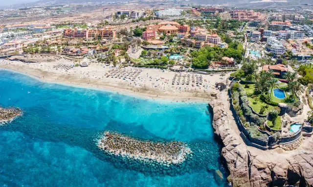 Widok z lotu ptaka na Costa Adeje plaże z turkusową wodą, piaszczystym brzegiem pełnym leżaków i palmami.