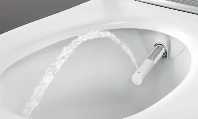 Chorro de agua saliendo de un inodoro moderno, mostrando la función de ducha integrada. Es como si el inodoro tuviera su propio bidet para quitar impurezas.
