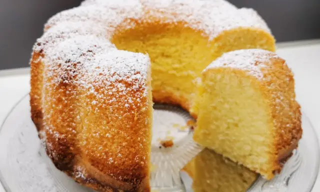 Wilgotna babka z ajerkoniakiem, oprószona cukrem pudrem, prezentuje się apetycznie na szklanej paterze.