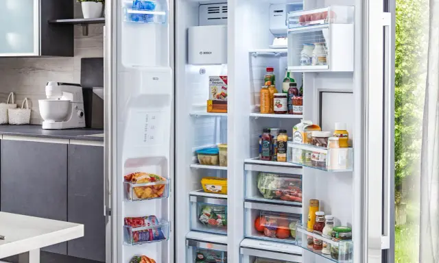 Offener Kühlschrank mit Lebensmitteln, darunter gefrorene Produkte und Getränke. Die Temperatur im Gefrierschrank ist ideal für die Lagerung.