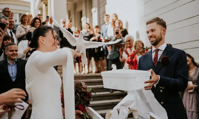Para młoda wypuszcza gołębie na kameralnym weselu. W tle widać gości z telefonami.