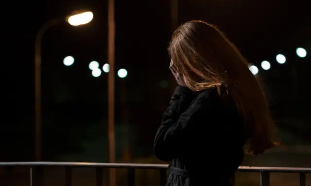 Kobieta z rudymi włosami, zakrywająca twarz dłońmi, stoi na balkonie nocą. W tle migoczą światła uliczne, symbolizujące stres przed seksem.