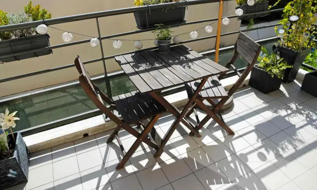 Un piccolo tavolo e sedie in legno su un balcone, con piante e lucine, perfetti per trasformare il balcone in terrazzo.