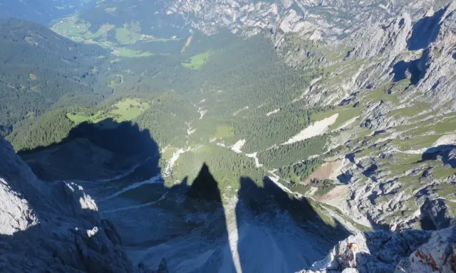 Ombra delle **Torri del Vajolet** che si allunga su un paesaggio alpino di boschi e valli verdi.