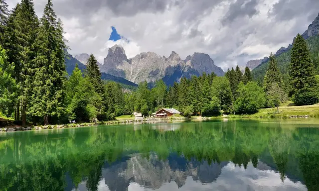 Riflessi perfetti sul lago Welsperg, con montagne maestose e una baita accogliente tra gli alberi.
