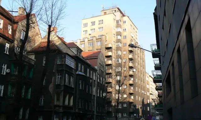 Wysoki, jasny drapacz chmur w Katowicach góruje nad starą kamienicą.