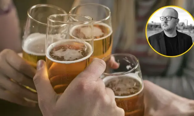 Ludzie wznoszą toasty piwem, podczas gdy w tle widać mężczyznę w okularach, który może symbolizować problem z alkoholem.