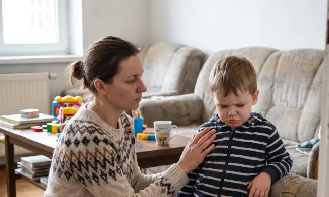 Mama uspokaja dziecko, które wpada w histerię z byle powodu. W tle widać kanapę i stolik z zabawkami.