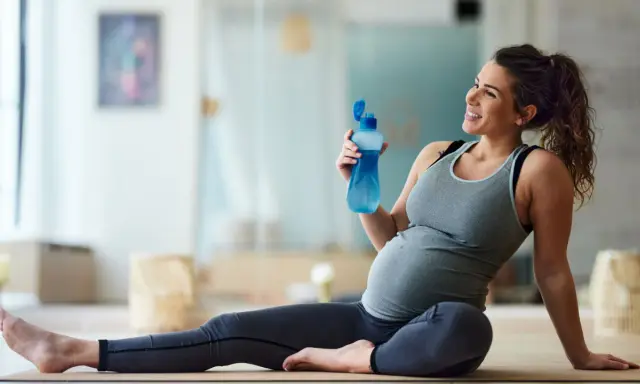 Donna incinta sorride con una bottiglia d'acqua dopo una sessione di yoga in gravidanza.
