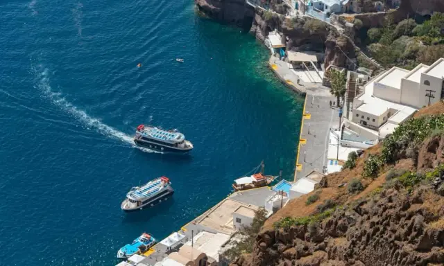 Barche turistiche navigano nel blu intenso del porto di Santorini, con le case bianche aggrappate alla scogliera.
