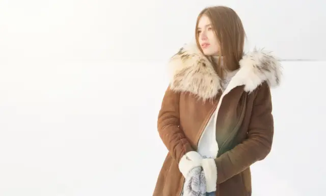 Mujer con abrigo de pelo natural en la nieve, lista para limpiar su ropa de invierno.