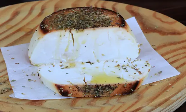 Ricotta al forno dorata e profumata con erbe aromatiche, servita su un tagliere di legno.