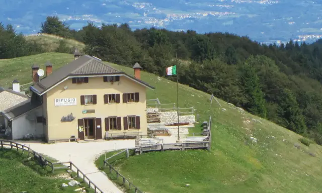Il rifugio Posa Puner, con la bandiera italiana che sventola, domina un paesaggio montano verdeggiante.