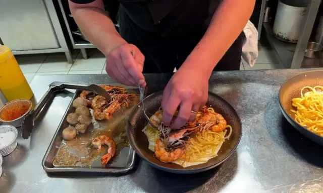 Un chef prépare des pâtes aux crevettes et pétoncles, un plat savoureux de cuisine de terroir.