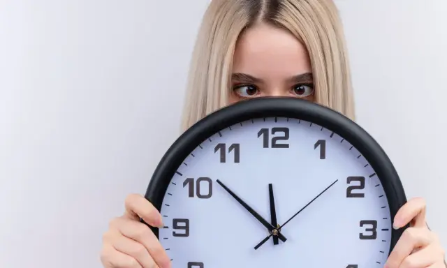 Dziewczyna z blond włosami ukrywa się za zegarem, patrząc zza niego. Czyżby czas miał dla niej jakieś szczególne 2233 znaczenie?