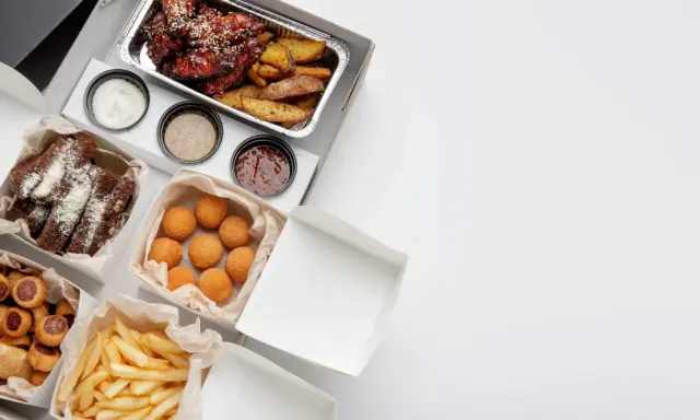 Variedad de comida para llevar: alitas, costillas, papas fritas, croquetas y pan. ¡Todo listo para disfrutar!