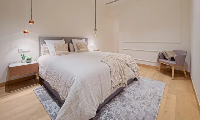Dormitorios relajantes con cama amplia, manta texturizada, sillón acogedor y luces colgantes.
