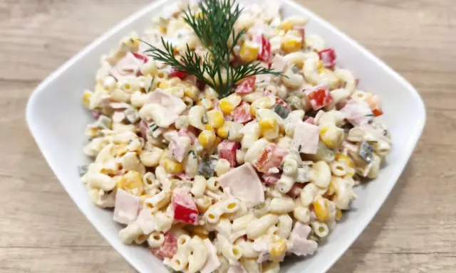Pyszna sałatka z makaronem i szynką, kukurydzą, papryką i ogórkiem, udekorowana gałązką koperku.