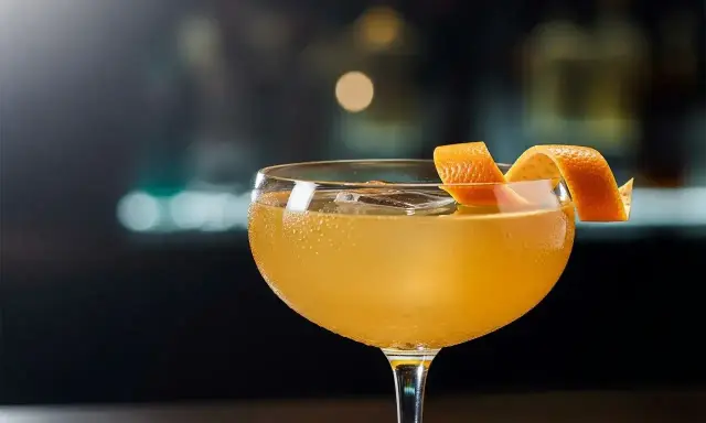 En gyllene cocktail i ett coupeglas, garnerad med en apelsinzest. Ett klassiskt, old fashioned recept som lockar.