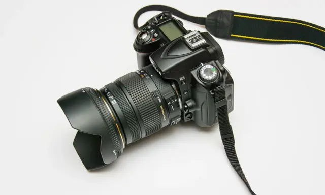 Czarny aparat fotograficzny z obiektywem i paskiem na białym tle.