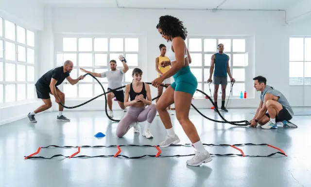 Gruppe trainiert mit Seilen und Leitern. Ein Mann gibt Anweisungen, während andere intensives Intervalltraining absolvieren.