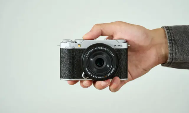Mano sujetando una cámara Fujifilm X-M5 plateada y negra, lista para capturar momentos.