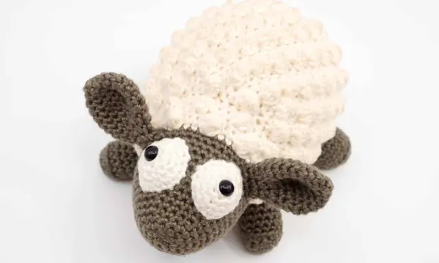 Oveja amigurumi de ganchillo con lana crema y marrón, ojos grandes y expresivos, lista para abrazar.