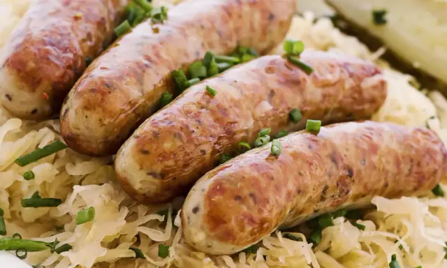 Aksamitna biała kiełbasa w kiszonej kapuście, posypana szczypiorkiem. Pyszne danie gotowe do podania.