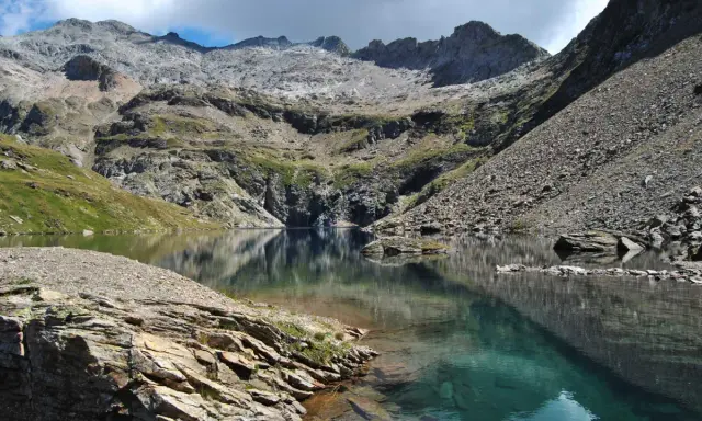 Riflessi perfetti sul lago nero, incastonato tra montagne rocciose e verdi pendii.