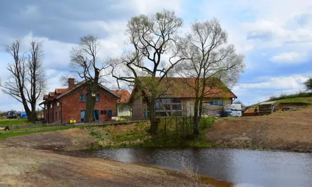Idealne miejsce gdzie na weekend we dwoje: urokliwe domki z cegły i drewna nad stawem, otoczone drzewami.