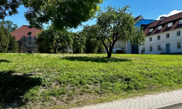 Zielona polana przed zabytkowymi budynkami, idealne miejsce na relaks i odkrywanie sztynort atrakcje.