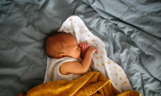 Noworodek śpi otulony kocykiem. Skóra dziecka ma lekko żółtawy odcień, co może sugerować żółtaczkę u dziecka.