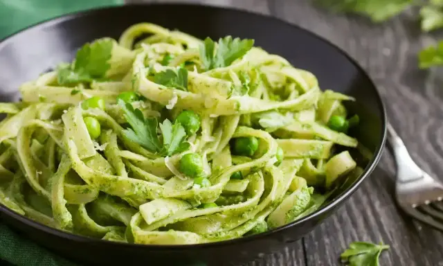 Pyszne tagliatelle z zielonym pesto, groszkiem i listkami pietruszki w czarnej misce.