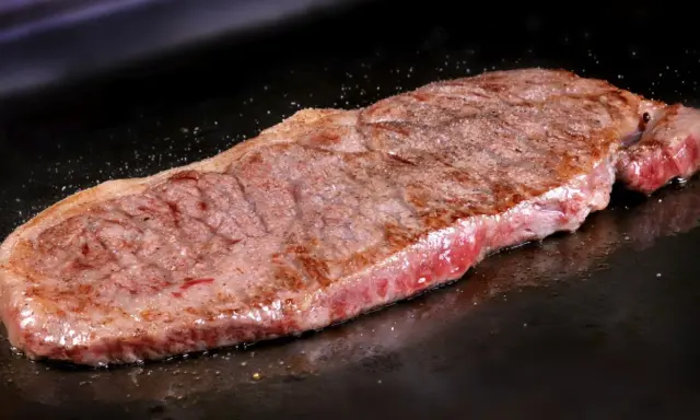 Un jugoso filete de ternera, recién hecho, con un borde dorado y un interior rosado, reposa sobre una plancha oscura.