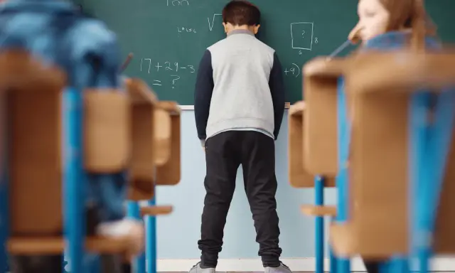 Chłopiec stoi przed tablicą z zadaniami matematycznymi.