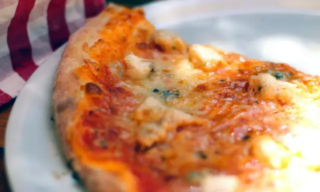 Tranche de pizza appétissante sur une assiette blanche, avec une serviette à carreaux rouges et blancs. Une recette parfaite avec de la farine sans gluten pour pizza.