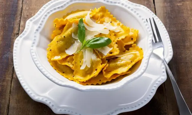 Un piatto invitante di tortelli di zucca, guarniti con scaglie di parmigiano e una fogliolina di basilico, pronti per essere gustati.