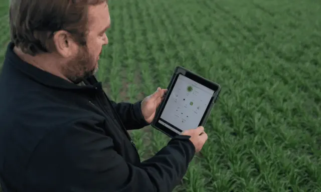 Farmer uses a tablet to monitor crop health and optimize yields, showcasing the power of digital farming in a lush green field.