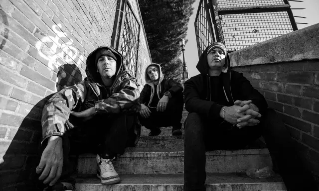 Tre uomini con cappuccio siedono sulle scale, un'atmosfera da musica hip hop famosa.