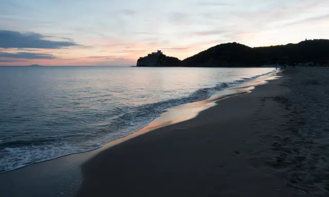 Tramonto sulla costa della Toscana, con un castello su una collina e il mare calmo. Un ricordo di vacanza con un neonato.