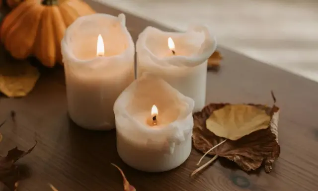 Candele accese su un tavolo di legno, con zucche e foglie autunnali. Un'ispirazione per chi vuole imparare come fare candele in casa.
