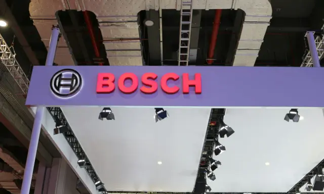 Logo Bosch i nazwa firmy na fioletowym tle. W tle widać instalacje przemysłowe, przewody i drabiny, sugerujące miejsce, gdzie odbywa się produkcja.