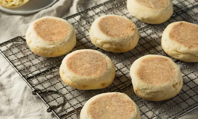 Plusieurs muffins anglais dorés et moelleux refroidissent sur une grille. Parfaits pour le petit-déjeuner.