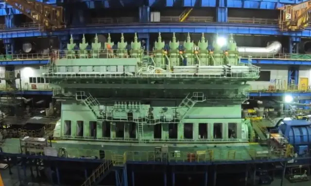 Un immense moteur vert, prêt à propulser un porte-conteneurs, se dresse dans un atelier de construction navale.