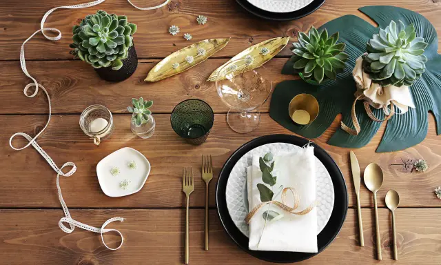 En vacker dukning med suckulenter, gyllene detaljer och gröna blad. En inbjudande och stilren bordsuppsättning.