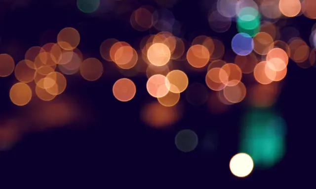 Rozmyte kule świateł, tworzące magiczny efekt bokeh w telefonie. Ciepłe pomarańcze i zielenie na ciemnym tle.