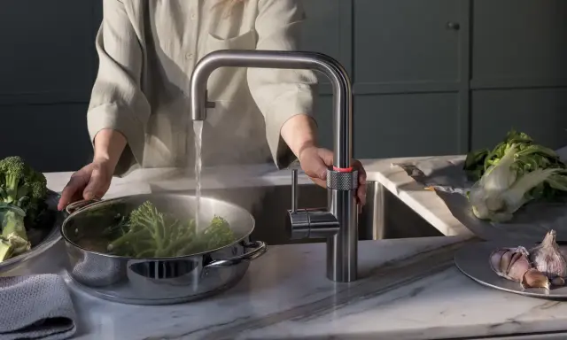 Person kocht Brokkoli mit heißem Wasser aus einem Quooker. Manche fragen sich, ob ein Quooker ungesund ist, aber hier wird er für gesunde Ernährung genutzt.