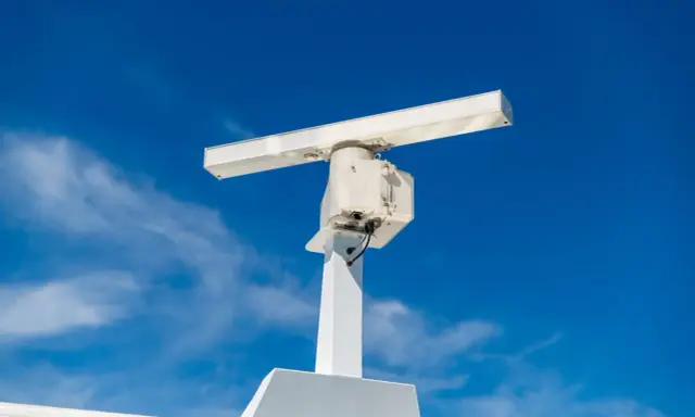 Antenne blanche sur un mât, sous un ciel bleu. Elle ressemble à un radar, mais pourrait aussi servir pour la communication satellite.